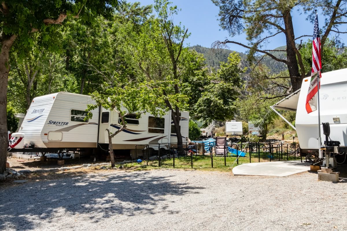 A fenced long-stay trailer site under shade trees
